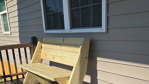 A wooden bench on a wooden deck with a house in the background.