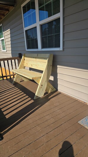 Un banco de madera en una terraza de madera, con una casa al fondo.