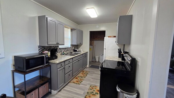 A compact kitchen with grey cabinets, a microwave, a stove, and a sink.