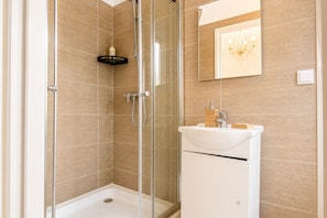 A modern bathroom with a glass-enclosed shower, a white sink with a soap dish, and a mirror with a chandelier.
