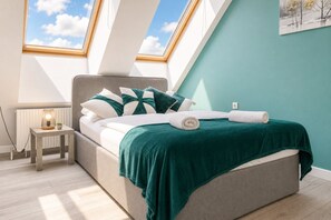 A bedroom with a skylight, a bed with a green blanket, and a small bedside table with a lamp.