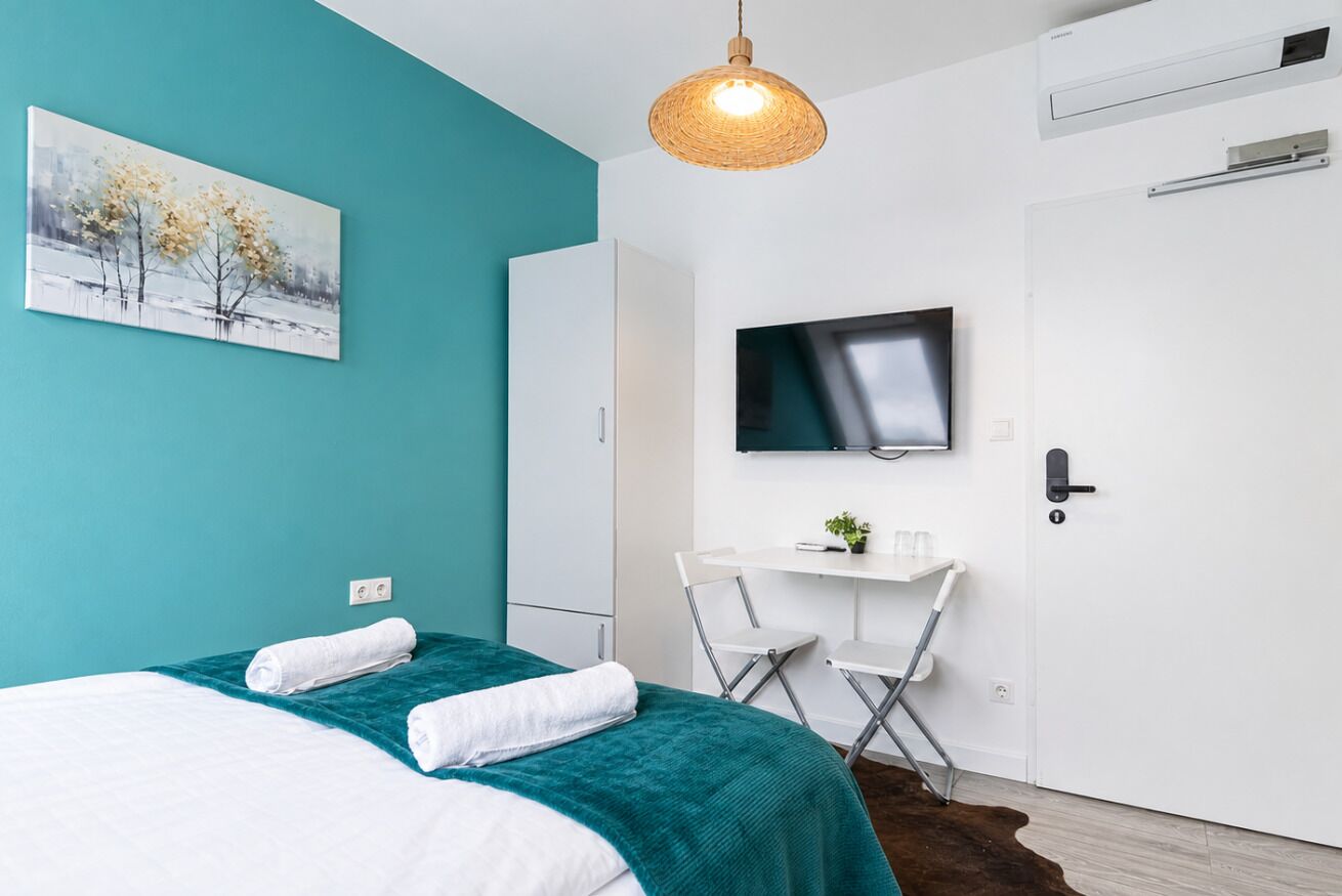 Ett modernt hotellrum med en säng, ett skrivbord, en tv och en tavla på väggen.