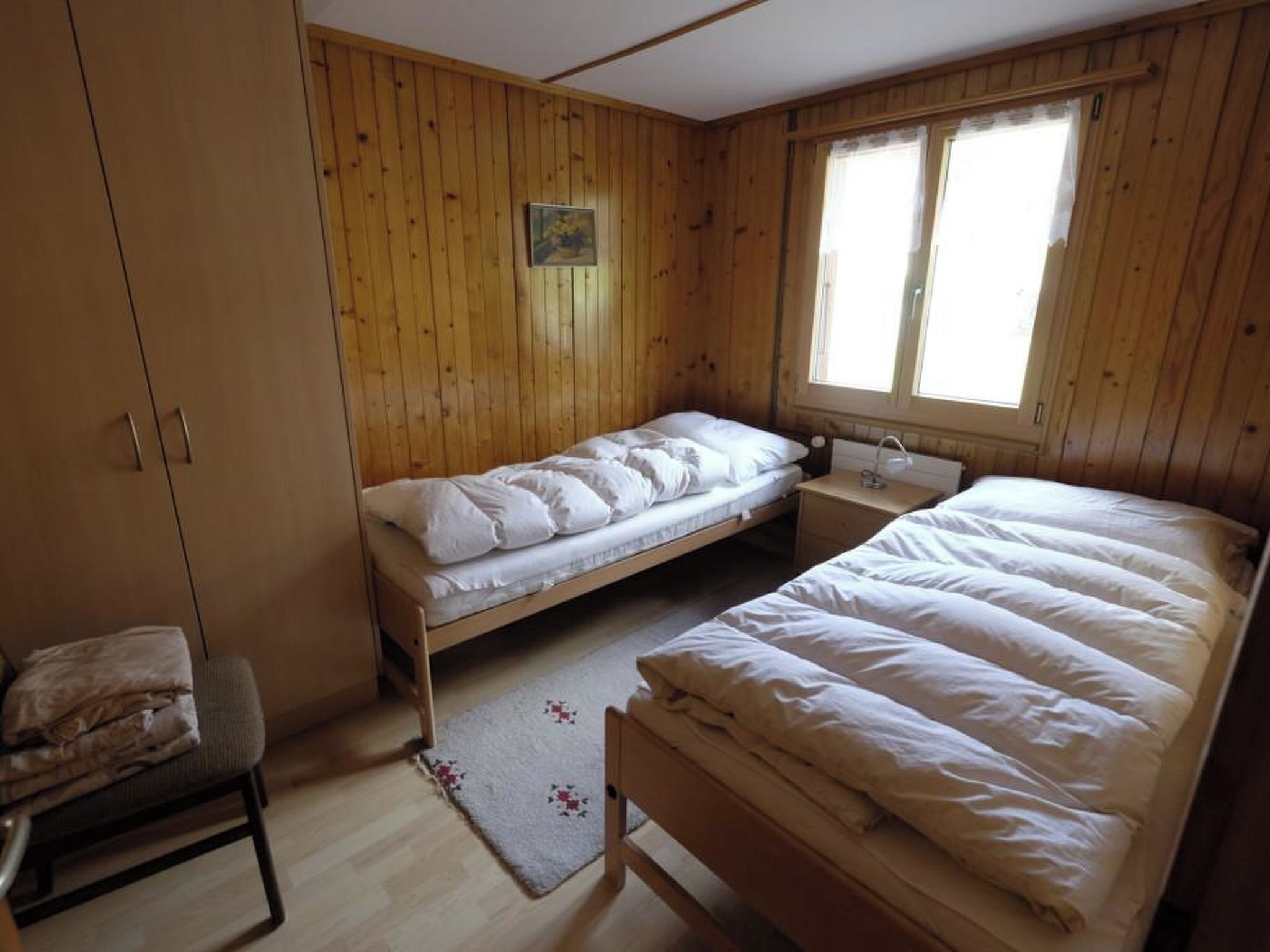 Ein Zimmer mit zwei Betten, einem Holzschrank, einem kleinen Tisch und einem Fenster.