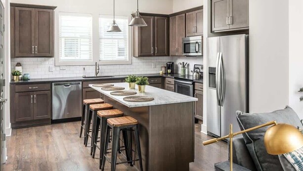 A modern kitchen with dark wood cabinets, a central island with stools, stainless steel appliances, and a pendant light. - E. Nash 3BR Escape | Walkable | Family Friendly (Nashville)