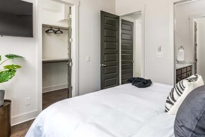 A bedroom with a bed, a television mounted on the wall, a plant, and a closet with a mirror. - E. Nash 3BR Escape | Walkable | Family Friendly (Nashville)