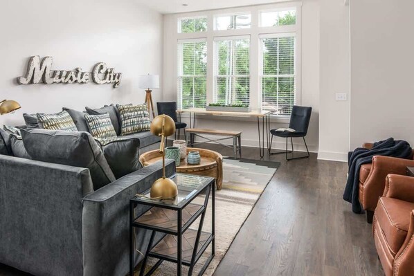 Un salon comprenant un canapé, des fauteuils, une table basse et une fenêtre avec des stores.