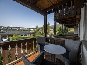 Un balcon doté de meubles en osier et d’une table, offrant une vue sur un quartier résidentiel avec des maisons et une montagne en arrière-plan.
