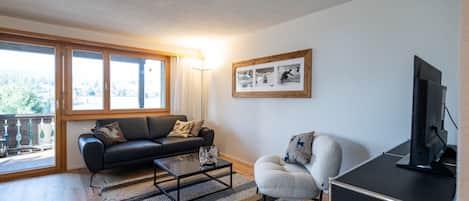 Una sala moderna con sofá, sillón, mesa de centro y televisor.