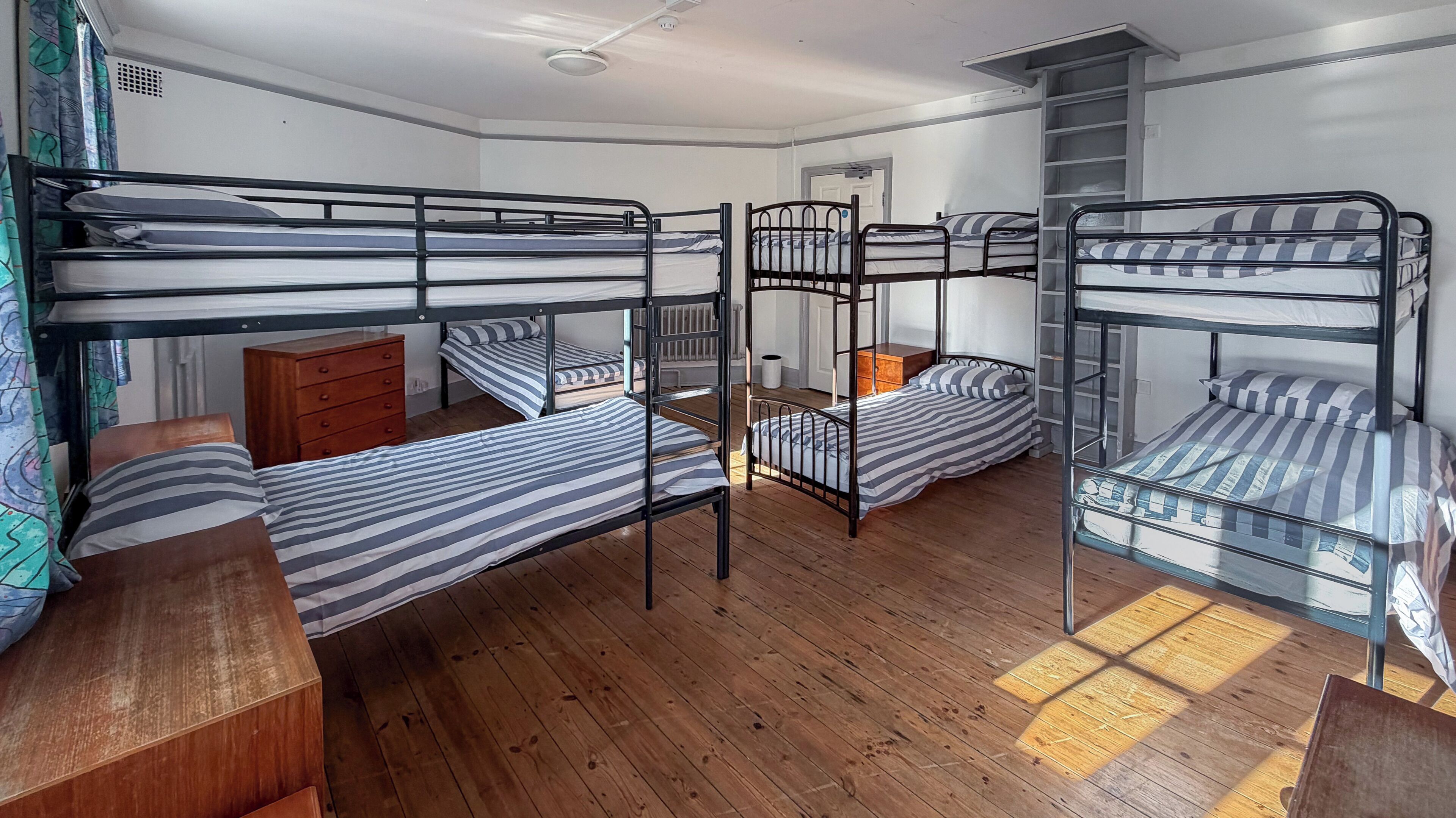 A dormitory room with bunk beds, wooden flooring, a dresser, and a radiator.