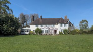 A large, two-story house with a white facade, multiple chimneys, and a green lawn in front.