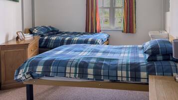 A bedroom with two beds, a wooden dresser, a bedside table, a window with curtains, and a sink.