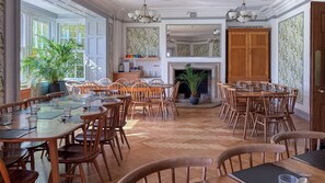 Un comedor amplio con múltiples mesas y sillas de madera, una chimenea y ventanas grandes que permiten la entrada de luz natural.