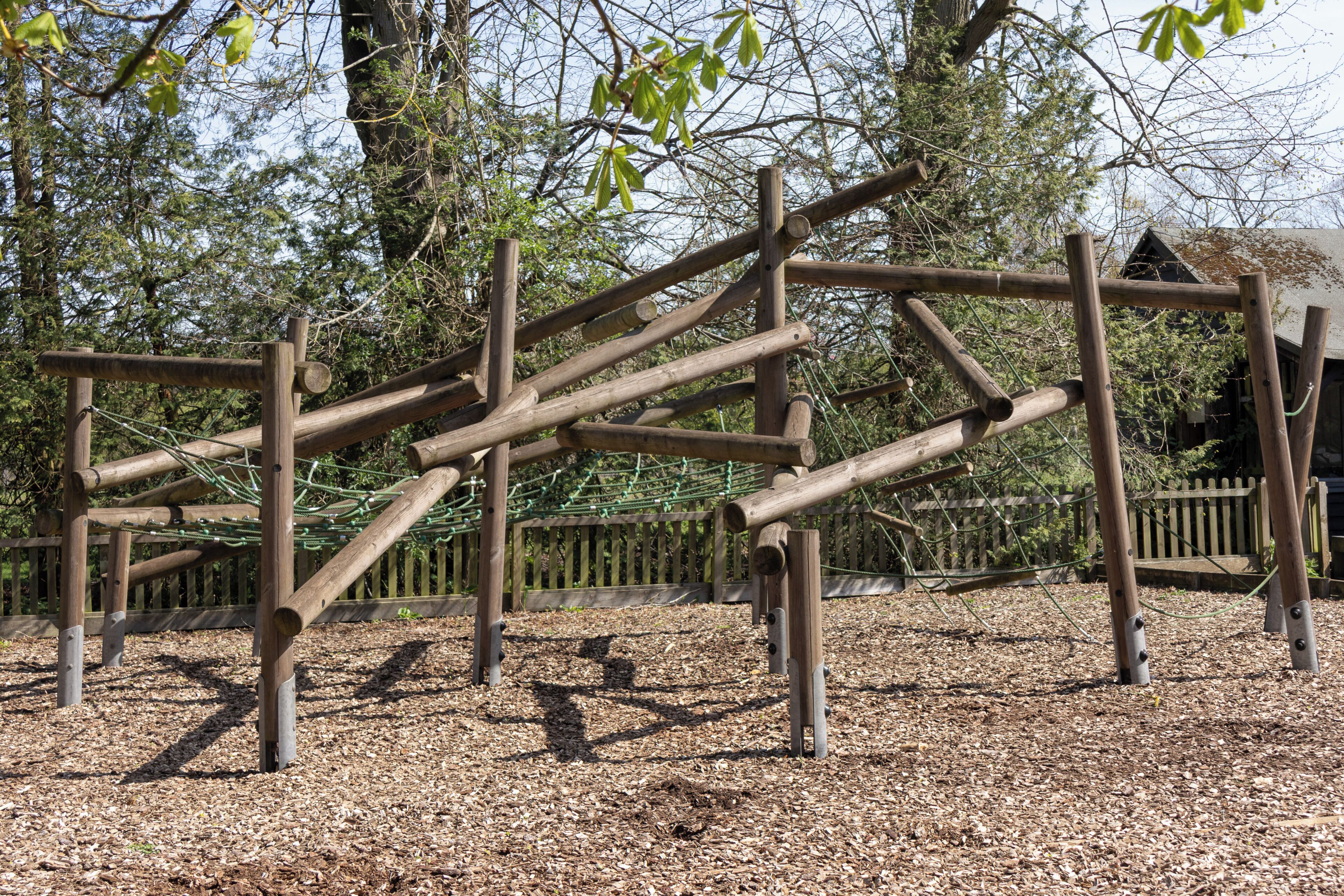 A playground with wooden climbing structures and a wooden fence in the background.