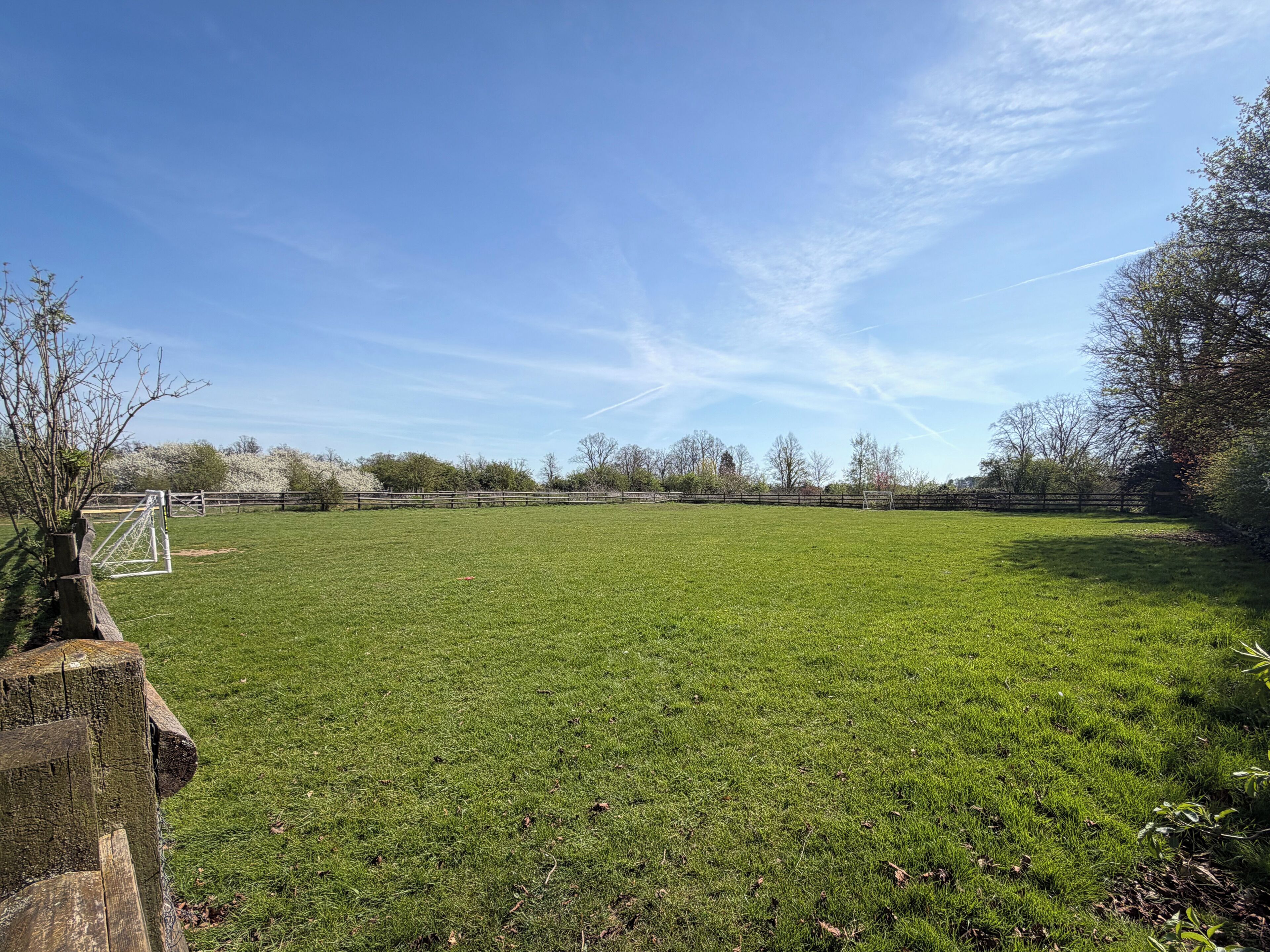 A grassy field with a goalpost and a wooden fence.