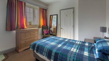 Un dormitorio con cama, cómoda, ventana con cortinas, puerta y mesita de noche con lámpara.
