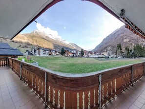 Blick vom Balkon auf eine gebirgige Landschaft mit Gebäuden und einer Rasenfläche.