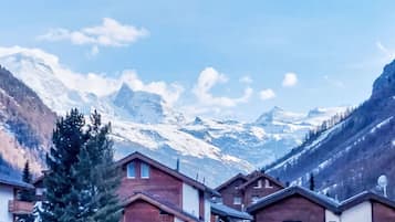 A mountain village with chalet-style houses, snow-covered peaks in the background, and a clear sky.