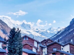 Ein Bergdorf mit Chalets, schneebedeckten Gipfeln im Hintergrund und blauem Himmel.