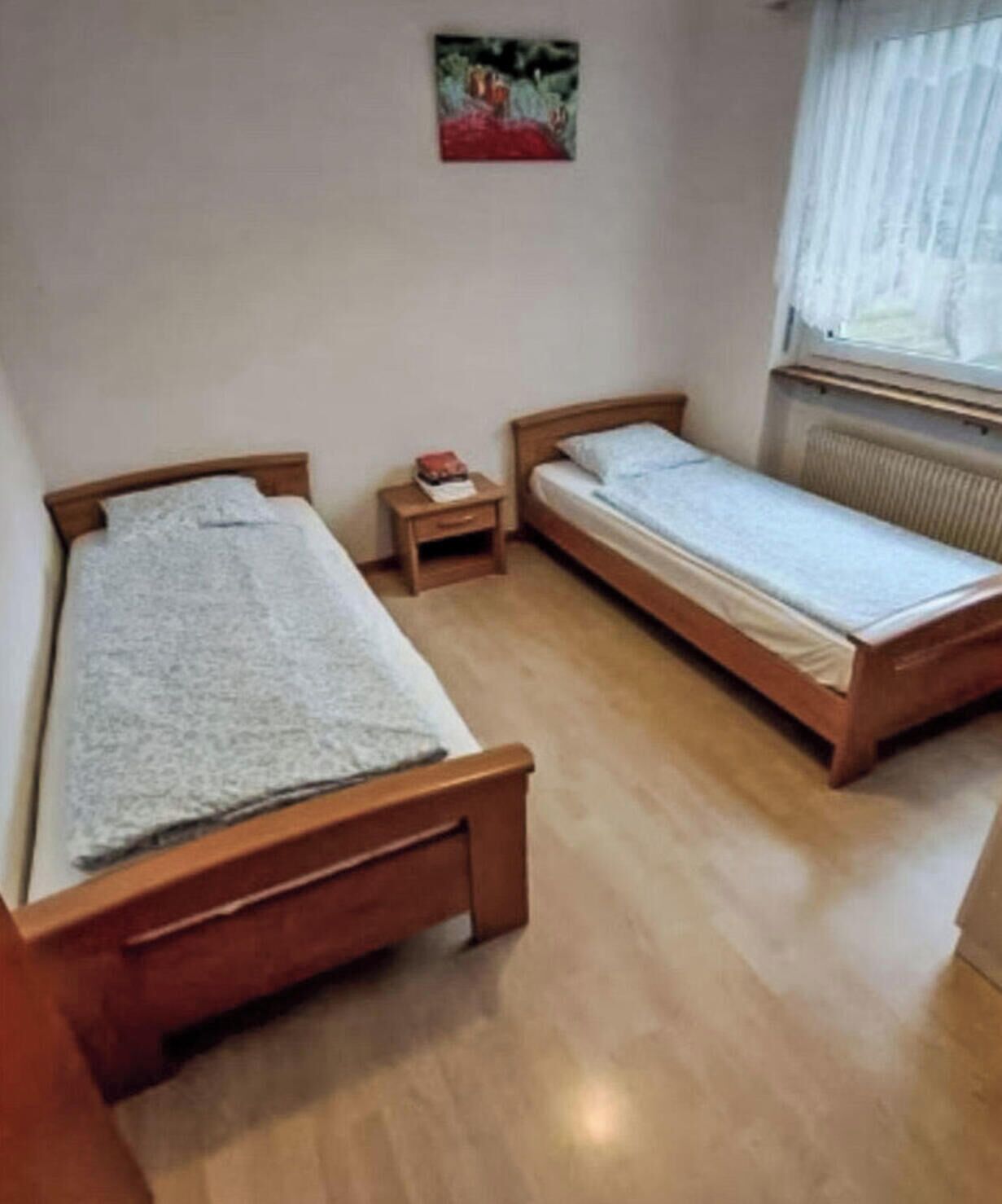 Une chambre avec deux lits en bois, une petite table de chevet sur laquelle se trouve un livre, et un radiateur.