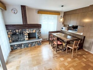 Una cocina con chimenea de piedra, suelo de madera y comedor con sillas.