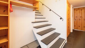 Una escalera con escalones de madera y barandilla, que conduce a un rellano con una estantería de madera.