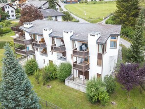A multi-story residential building with balconies, a paved driveway, and surrounding greenery.