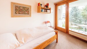 Un dormitorio con cama, una estantería, una silla y un ventanal grande.