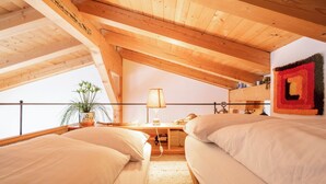 Un dormitorio acogedor en el ático con dos camas, un escritorio y una ventana que da a un balcón.