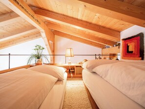 Ein gemütliches Schlafzimmer im Dachgeschoss mit zwei Betten, einem Schreibtisch und einem Fenster mit Blick auf einen Balkon.