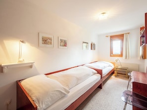 A room with two single beds, a desk, a chair, and a window with curtains.