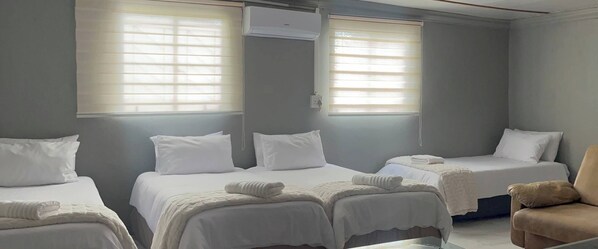 A hotel room with two single beds, a chair, and a window with blinds.