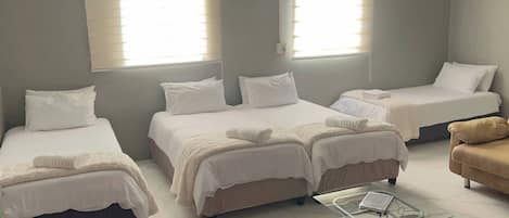 A hotel room with three beds, a sofa, a glass coffee table, and an air conditioning unit.