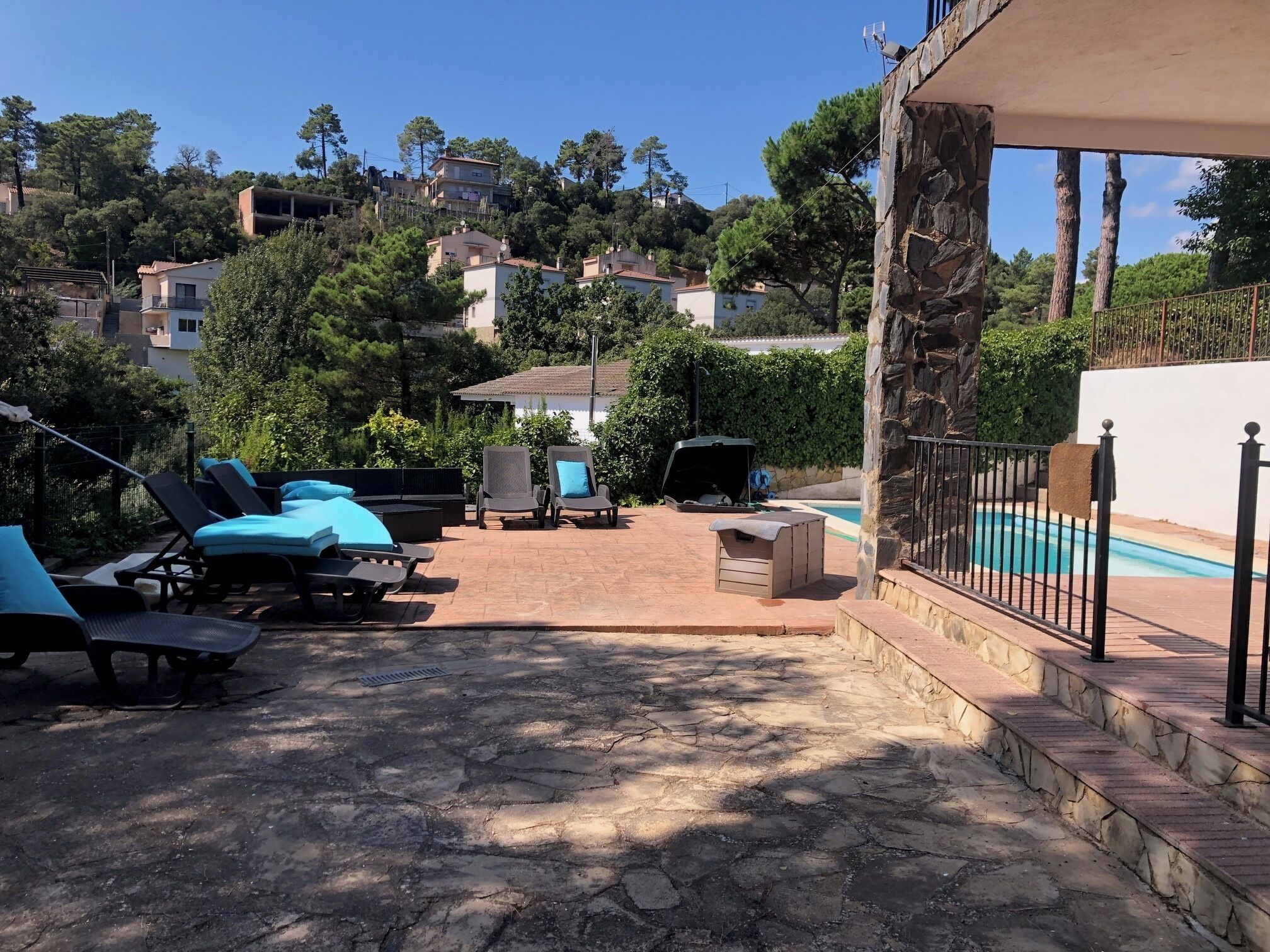Un patio con sillones de descanso y una parrilla, con vistas a una piscina y una colina con edificios.