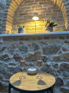 A table with two glasses of champagne, a candle, and a decorative bowl against a stone wall with a brick archway and a hanging lamp. - The Hidden Courtyart Studio | Dedicated Outdoor Area | Sleeps 3 (Vironas)
