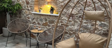 A stone wall with a built-in fireplace, wicker chairs, and a hanging swing chair.