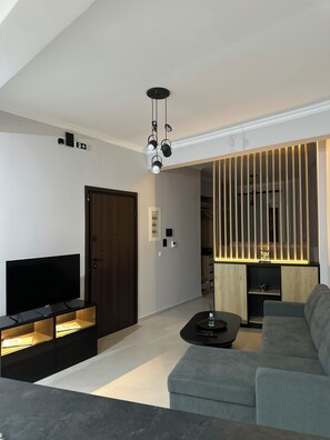A modern living room with a flat-screen TV, a sofa, a coffee table, and a unique lighting fixture. - The Hidden Courtyart Studio | Dedicated Outdoor Area | Sleeps 3 (Vironas)