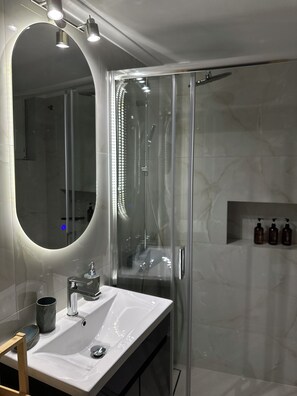 A modern bathroom with a glass shower enclosure, a white sink, and a mirror with integrated lighting. - The Hidden Courtyart Studio | Dedicated Outdoor Area | Sleeps 3 (Vironas)