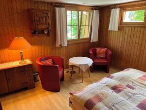 A wooden-paneled room with a bed, two red chairs, a small table, a lamp, and a cabinet. - Im Rägeboge Appartement/Fewo, Dusche, WC, 1 Schlafraum by Interhome (Adelboden)