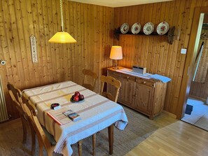 A wooden-paneled room with a dining table, chairs, a lamp, a laptop, and a shelf with decorative plates. - Im Rägeboge Appartement/Fewo, Dusche, WC, 1 Schlafraum by Interhome (Adelboden)