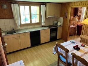 A kitchen with wooden cabinets, a granite countertop, a sink, and a dining area with a table and chairs. - Im Rägeboge Appartement/Fewo, Dusche, WC, 1 Schlafraum by Interhome (Adelboden)