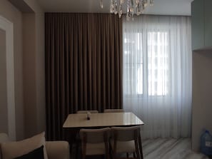 A dining area with a table and chairs, a chandelier, and a window with sheer curtains. - Baku Avant Park Premium (Baku)
