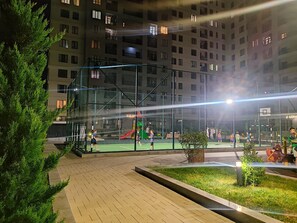 An outdoor sports facility with a basketball court, surrounded by a fence, and adjacent to a residential building. - Baku Avant Park Premium (Baku)