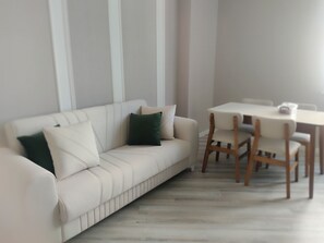 En stilren stue med en hvid sofa, grønne puder og et træspisebord med stole.