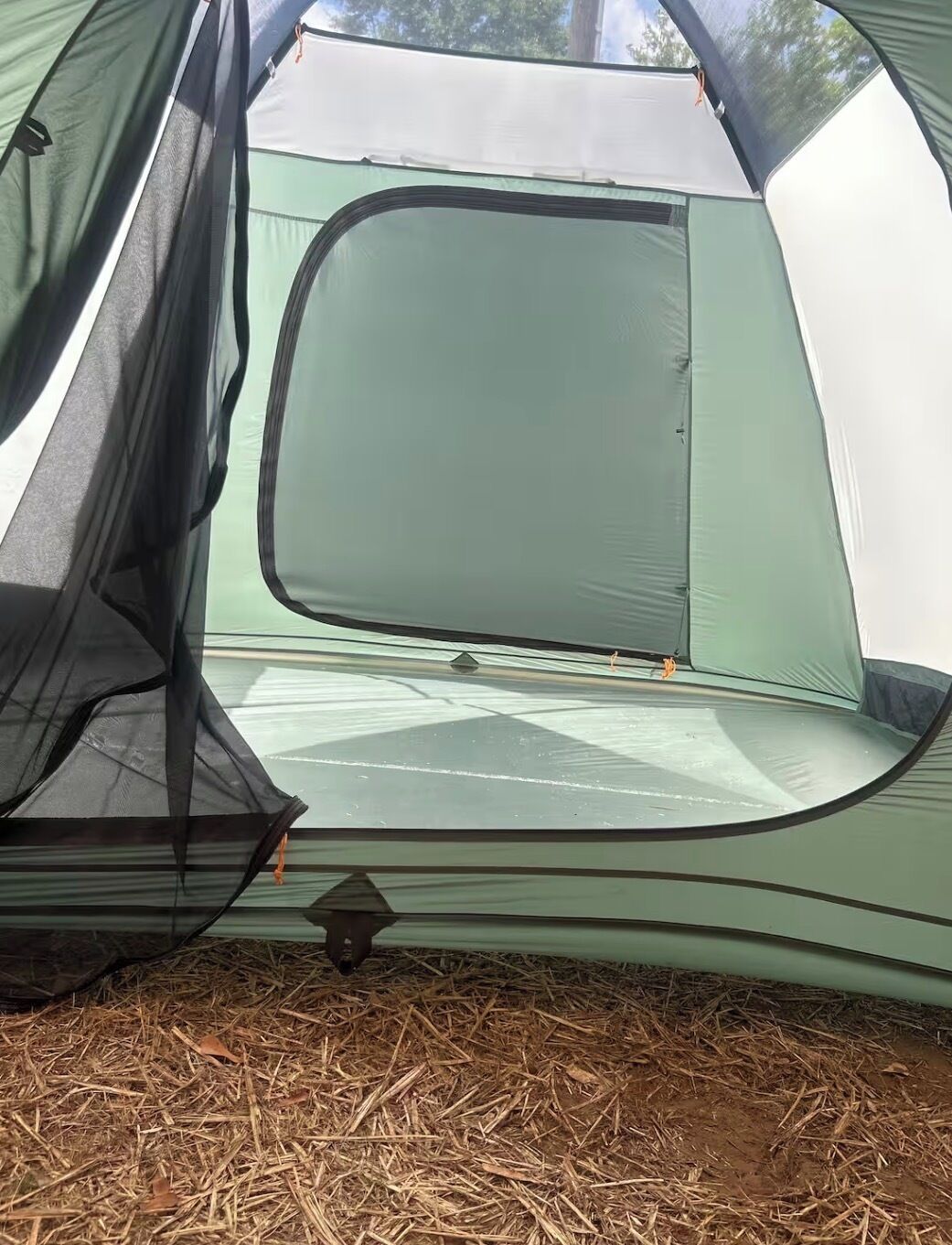 A tent with a mesh window, a sleeping area, and a ground covered with straw.