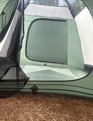 A tent with a mesh window, a sleeping area, and a ground covered with straw. - Tent in Leland perfect for your outdoor getaway (Leland)