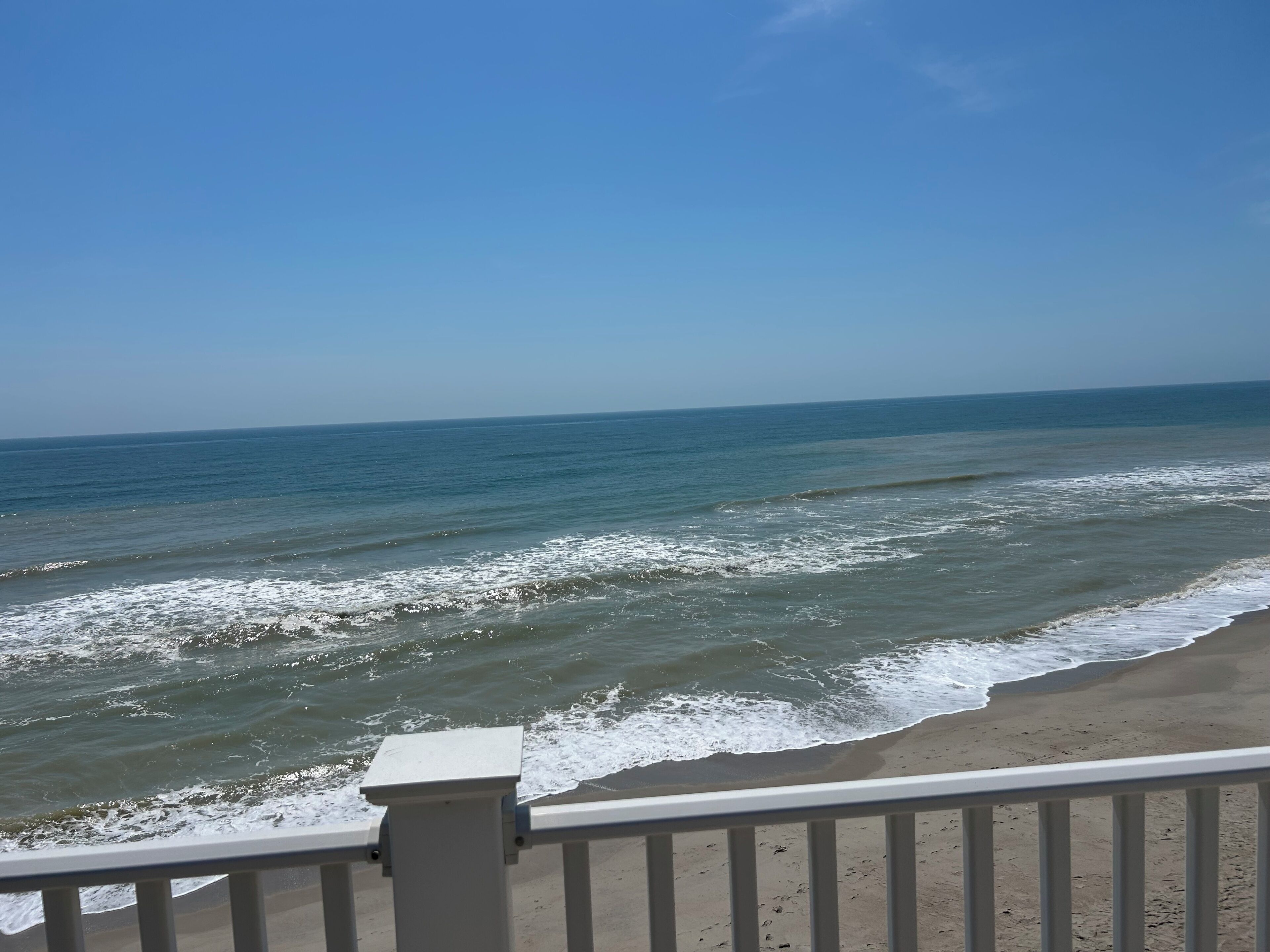 A beach view with waves, a clear sky, and a railing.