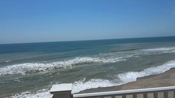A beach view with waves, a clear sky, and a railing.