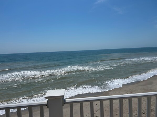 A beach view with waves, a clear sky, and a railing.