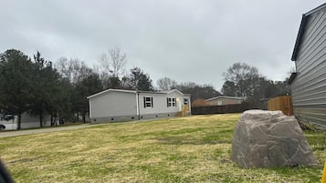 A residential area with a house, a large rock, and a wooden fence.