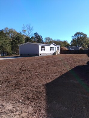 A single-story mobile home with a front porch and a fenced yard.
